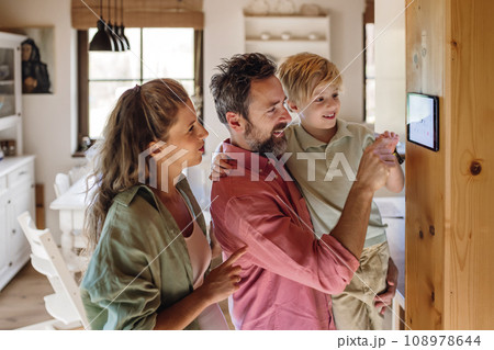 Family looking at smart thermostat, adjusting, lowering heating temperature at home. Concept of sustainable, efficient, and smart technology in home heating and thermostats. 108978644
