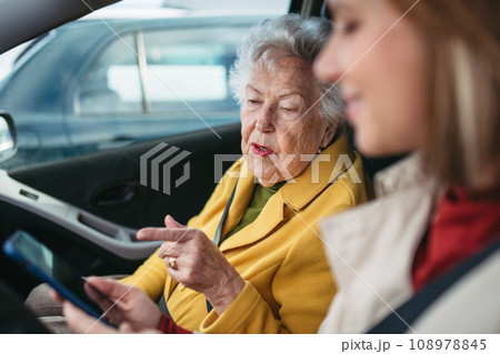 Granddaughter driving her elderly grandmother in the car, taking her to the doctor, shopping or to the bank. Caregiver driving elderly lady to the church, pharmacy, searching for route on a smartphone 108978845