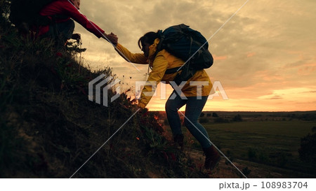 Tired woman with backpack climbs on hill top with friend help in autumn park 108983704