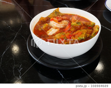 Deep fried egg with cha om leaves or Acacia omelets and fresh shrimp in sour curry soup in a white bowl, Asian traditional food style in Thailand 108984689