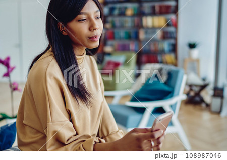 pretty pensive hipster girl chatting via application on mobile phone during free time 108987046