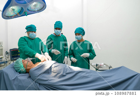 Group of surgeons, steeped in concentration, performing complex surgery in operating room. Sterile surgical instruments pepper the surrounding space, while monitors display vital patient data. Group of surgeons, steeped in concentration, performing complex surgery in operating room. Sterile surgical instruments pepper the surrounding space, while monitors display vital patient data. 108987881