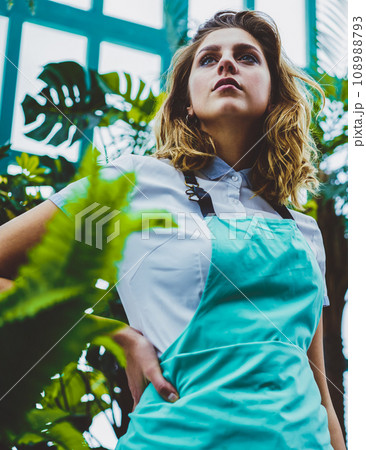contemplative caucasian woman in casual apron looking away in warmhouse 108988793