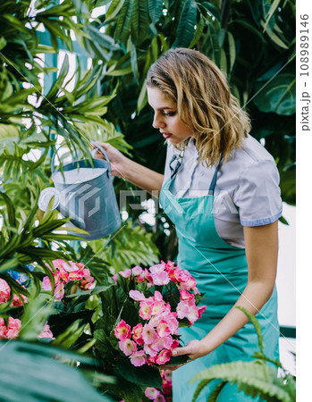 Professional female employee of orangery watering flowers with can and taking care of plants 108989146