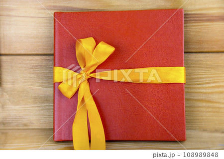 Red book with yellow ribbon. Red gift on a wooden background. Red book with yellow ribbon. Red gift on a wooden background. 108989848