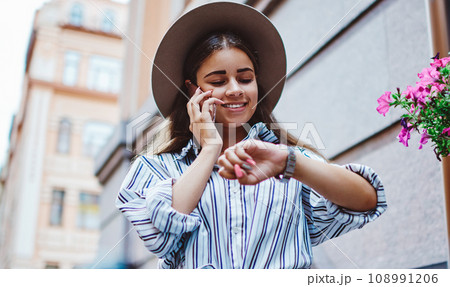smiling hipster girl making telephone calling roaming looking at clock arranging meeting smiling hipster girl making telephone calling roaming looking at clock arranging meeting 108991206