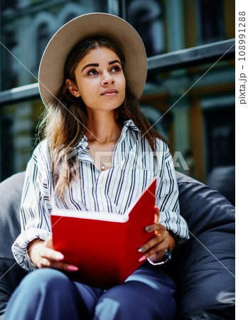 pensive hipster girl sitting outdoors with book looking up 108991288