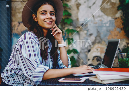 Young hipster girl sitting with laptop computer at cafe on street satisfied with idea for blog 108991420