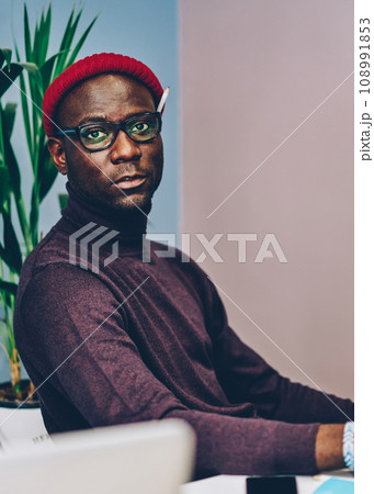 serious dark skinned employee looking at camera during workflow on creating plan serious dark skinned employee looking at camera during workflow on creating plan 108991853