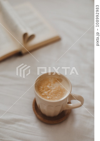 Cozy morning composition with a coffee cup and a book with pages folded into a heart shape in bed 108992983