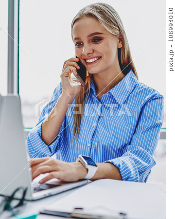 Successful young woman calling on mobile phone during remote work at laptop Successful young woman calling on mobile phone during remote work at laptop 108993010