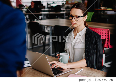 concentrated female finance manager sitting at working space with laptop for browsing 108993176
