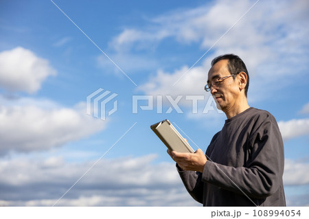 屋外でタブレットを持って立っている中高年男性 108994054