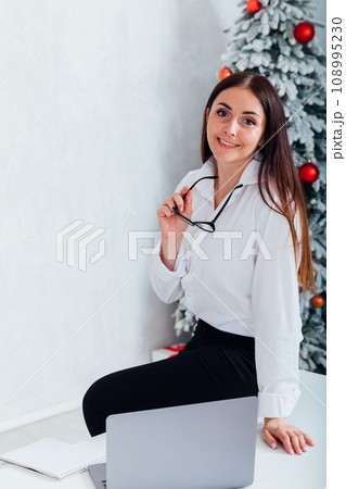 Young happy spanish businesswoman using smartphone while working laptop at home on Christmas 108995230