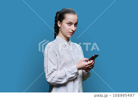 Young teenage female with smartphone on blue background 108995497