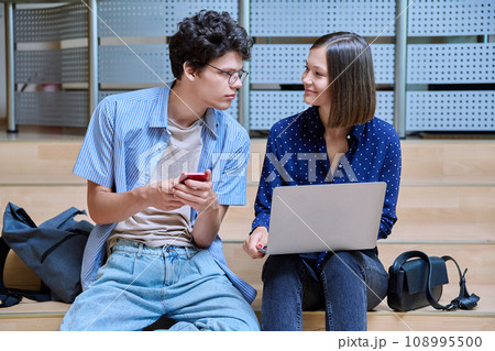 Friends college students guy and girl with smartphone laptop inside educational building 108995500