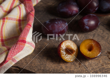 Whole and half of purple plums on wooden background. . 108996346