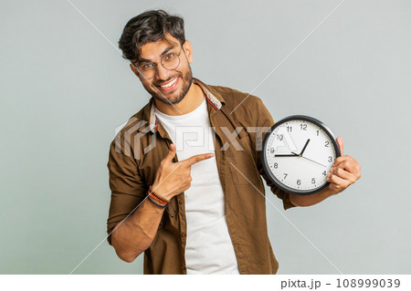 Indian young man showing time hour on wall office clock, ok, thumb up, approve, hurry up, deadline 108999039