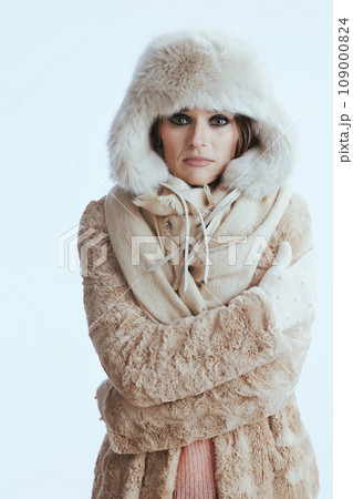 sad modern woman in winter coat and fur hat shivering on white 109000824