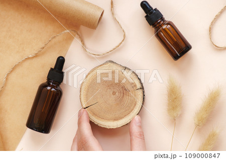 Hand making DIY scene. Glass amber bottles with black cap flat lay. Beauty products packaging. Dropper bottle with pipette on wooden podium. Natural eco-friendly cosmetics presentation with copy space 109000847