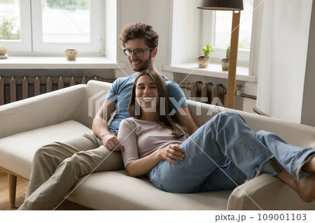 Couple laughing relaxing together on cozy couch in living room Couple laughing relaxing together on cozy couch in living room 109001103