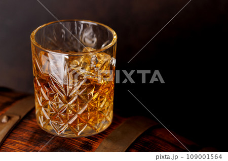 Whiskey glass with ice on a rustic barrel, a classic sip 109001564