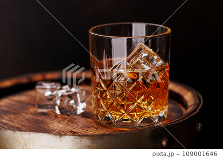 Whiskey glass with ice on a rustic barrel, a classic sip Whiskey glass with ice on a rustic barrel, a classic sip 109001646