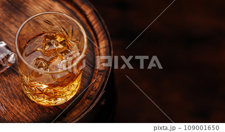 Whiskey glass with ice on a rustic barrel, a classic sip 109001650