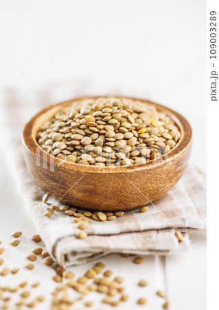 Uncooked lentil legumes in bowl on white table. 109003289