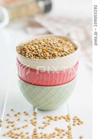 Uncooked lentil legumes in bowl on white table. 109003292