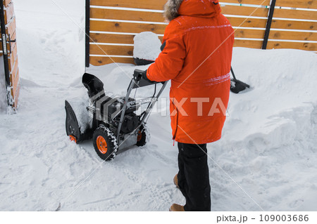 A man clear snow from backyard with snow blower. Winter season and snow blower equipment A man clear snow from backyard with snow blower. Winter season and snow blower equipment 109003686