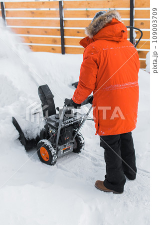 A man clear snow from backyard with snow blower. Winter season and snow blower equipment A man clear snow from backyard with snow blower. Winter season and snow blower equipment 109003709