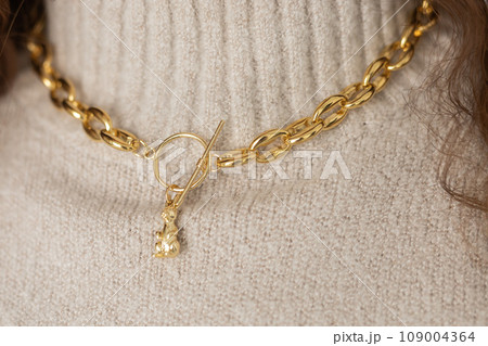 Close-up female in modern gold metal necklace chain with gold bunny pendant Close-up female in modern gold metal necklace chain with gold bunny pendant 109004364