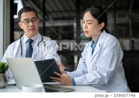 Young female doctor is asking for advice from a professional senior male doctor in the office room. Young female doctor is asking for advice from a professional senior male doctor in the office room. 109007746
