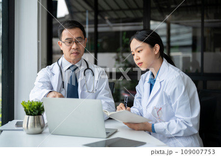 Young female doctor is asking for advice from a professional senior male doctor in the office room. Young female doctor is asking for advice from a professional senior male doctor in the office room. 109007753