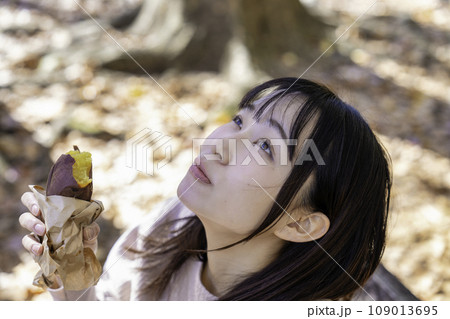 公園で焼き芋を食べる若い女性 109013695