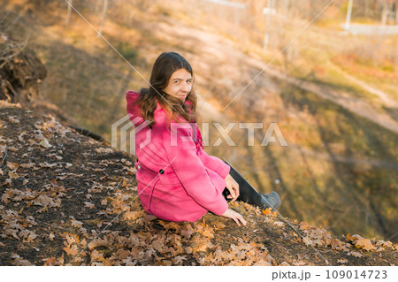 Beautiful happy smiling girl with long hair wearing pink jacket posing in autumn park. Outdoor portrait day light. Autumn mood concept. Generation Z and gen z youth. Copy empty space for text. Beautiful happy smiling girl with long hair wearing pink jacket posing in autumn park. Outdoor portrait day light. Autumn mood concept. Generation Z and gen z youth. Copy empty space for text. 109014723