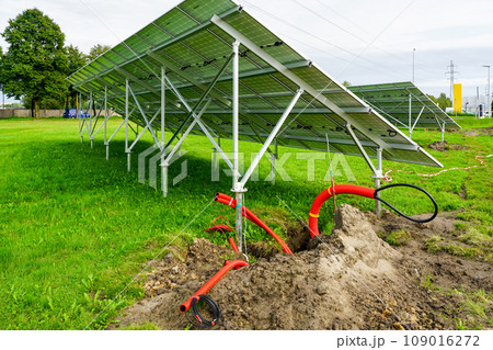 Installation of solar panels on metal frames in a green meadow, unfinished solar power plant Installation of solar panels on metal frames in a green meadow, unfinished solar power plant 109016272