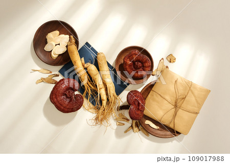 Scene for advertising traditional Chinese medicine with dried herbs decorated on white background. Fresh ginseng root, lingzhi mushrooms and medicine ladder wrapped in paper displayed 109017988