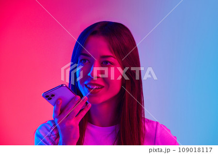 Young woman talking on mobile phone against gradient pink blue studio background in neon light. Communication Young woman talking on mobile phone against gradient pink blue studio background in neon light. Communication 109018117