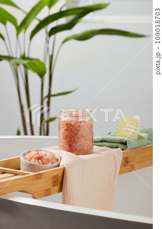 Wooden bathtub tray featured a glass jar and ceramic bowl of pink himalayan salt and a scalp massage brush. Pink himalayan salt often has larger crystals than table salt Wooden bathtub tray featured a glass jar and ceramic bowl of pink himalayan salt and a scalp massage brush. Pink himalayan salt often has larger crystals than table salt 109018703