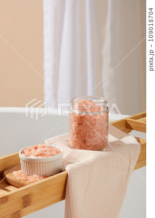 Close up view of a bowl and transparent jar containing pink himalayan salt placed on a wooden bathtub tray. Pink himalayan salt is a brilliant natural exfoliator Close up view of a bowl and transparent jar containing pink himalayan salt placed on a wooden bathtub tray. Pink himalayan salt is a brilliant natural exfoliator 109018704