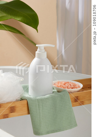 Pump bottle in white color decorated with a bath sponge and a small dish of pink himalayan salt. White cosmetic bottle for face cream, cleanser, body lotion or shampoo 109018706