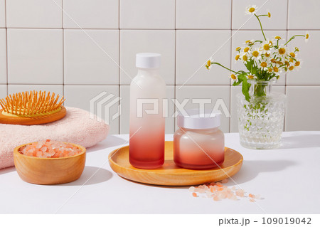 Unbranded jar and bottle in red gradient color decorated with a brush, a bowl of pink himalayan salt and flower pot. Front view. Skin care concept with organic ingredient 109019042