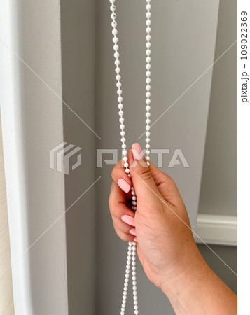 A female hand holding a beaded chain for the blinds. High quality photo 109022369