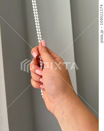 A female hand holding a beaded chain for the blinds. High quality photo A female hand holding a beaded chain for the blinds. High quality photo 109022374