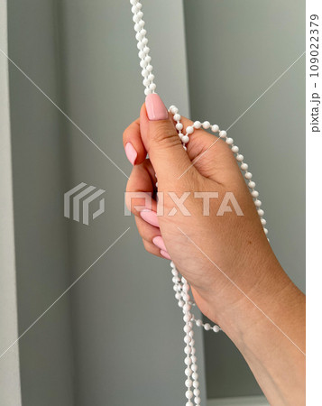 A female hand holding a beaded chain for the blinds. High quality photo 109022379