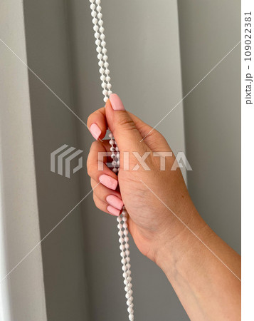A female hand holding a beaded chain for the blinds. High quality photo A female hand holding a beaded chain for the blinds. High quality photo 109022381