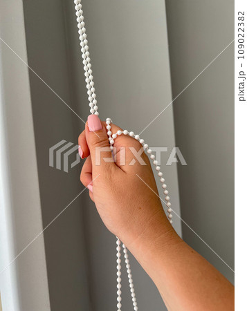 A female hand holding a beaded chain for the blinds. High quality photo 109022382