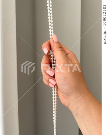 A female hand holding a beaded chain for the blinds. High quality photo 109022383